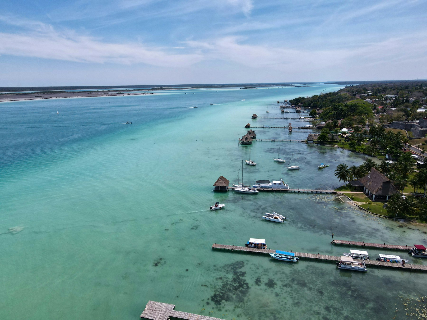 Aerial view of Bacalar Lagoon — the Lake of Seven Colors — with bands of blue and turquoise water and small piers along the shore.