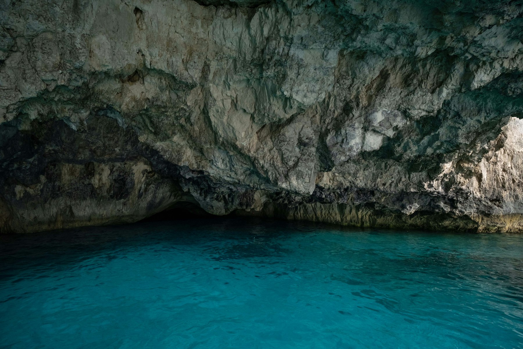 A vast cavern cenote near Tulum, with turquoise water reflecting off limestone walls beneath a soaring rock ceiling.