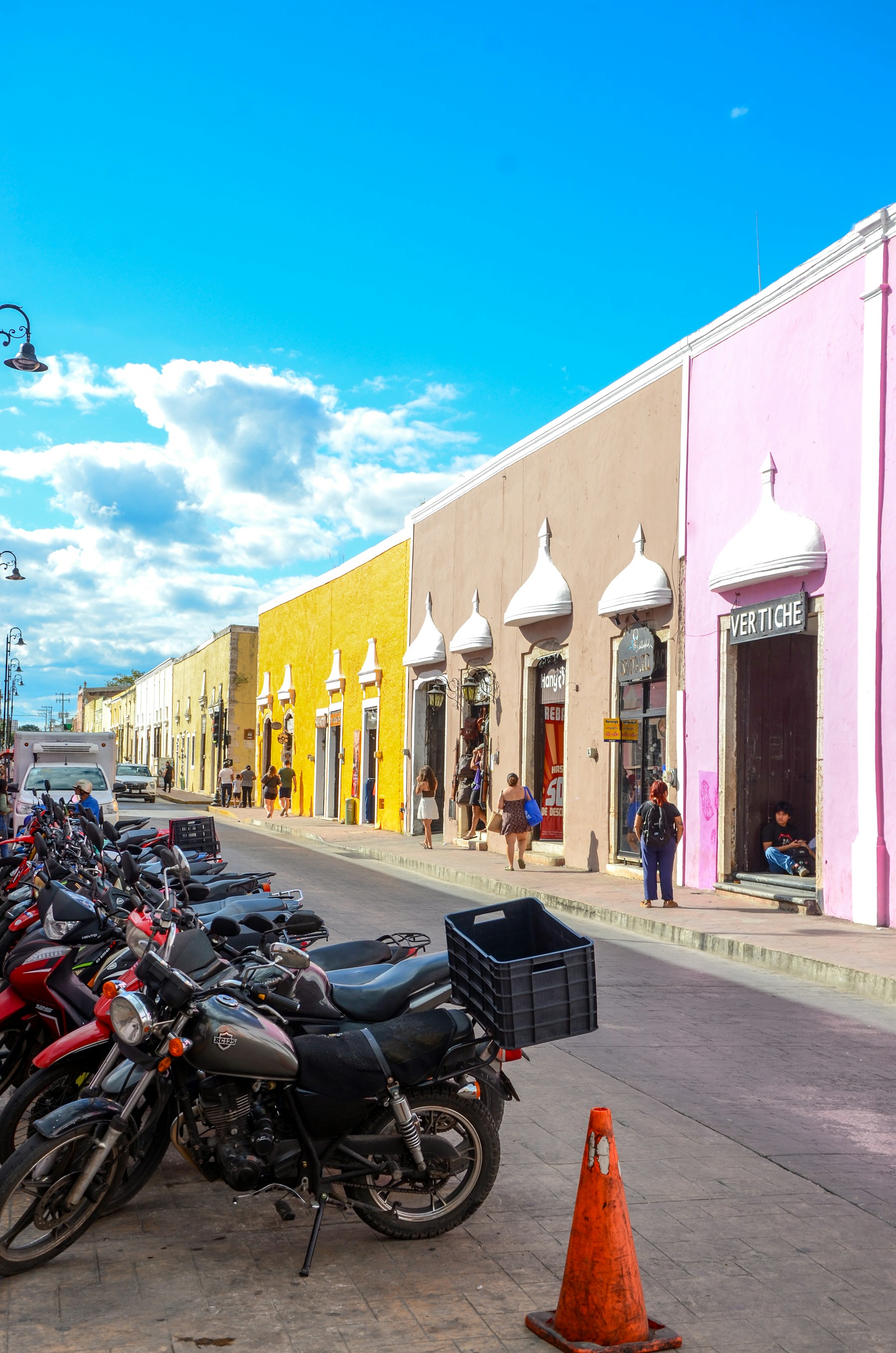 A colorful street in Valladolid, Yucatán, lined with yellow, rose, and beige colonial buildings under a bright blue sky.
